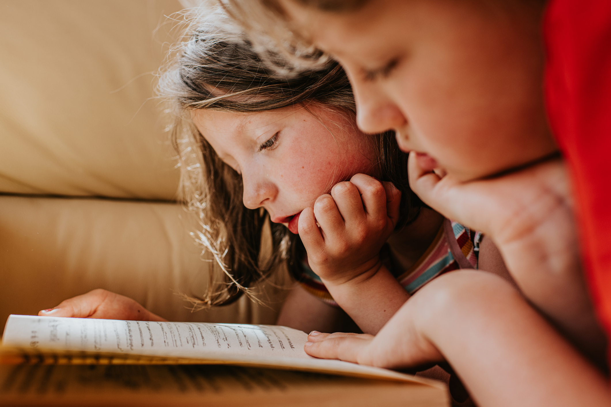 Two children are closely reading a book together, focused and engaged