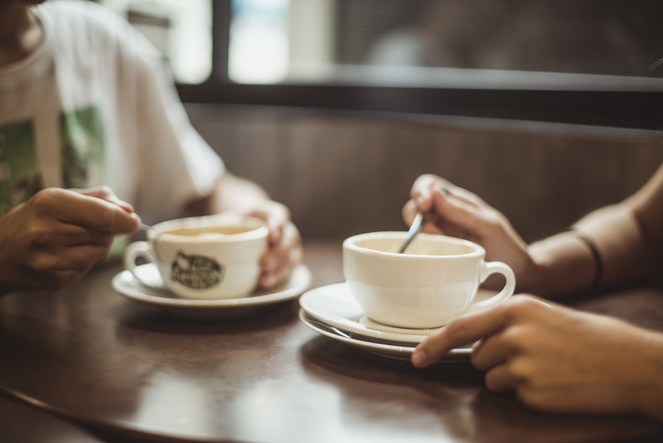 Two people sitting at a table, each holding a coffee cup, engaged in conversation