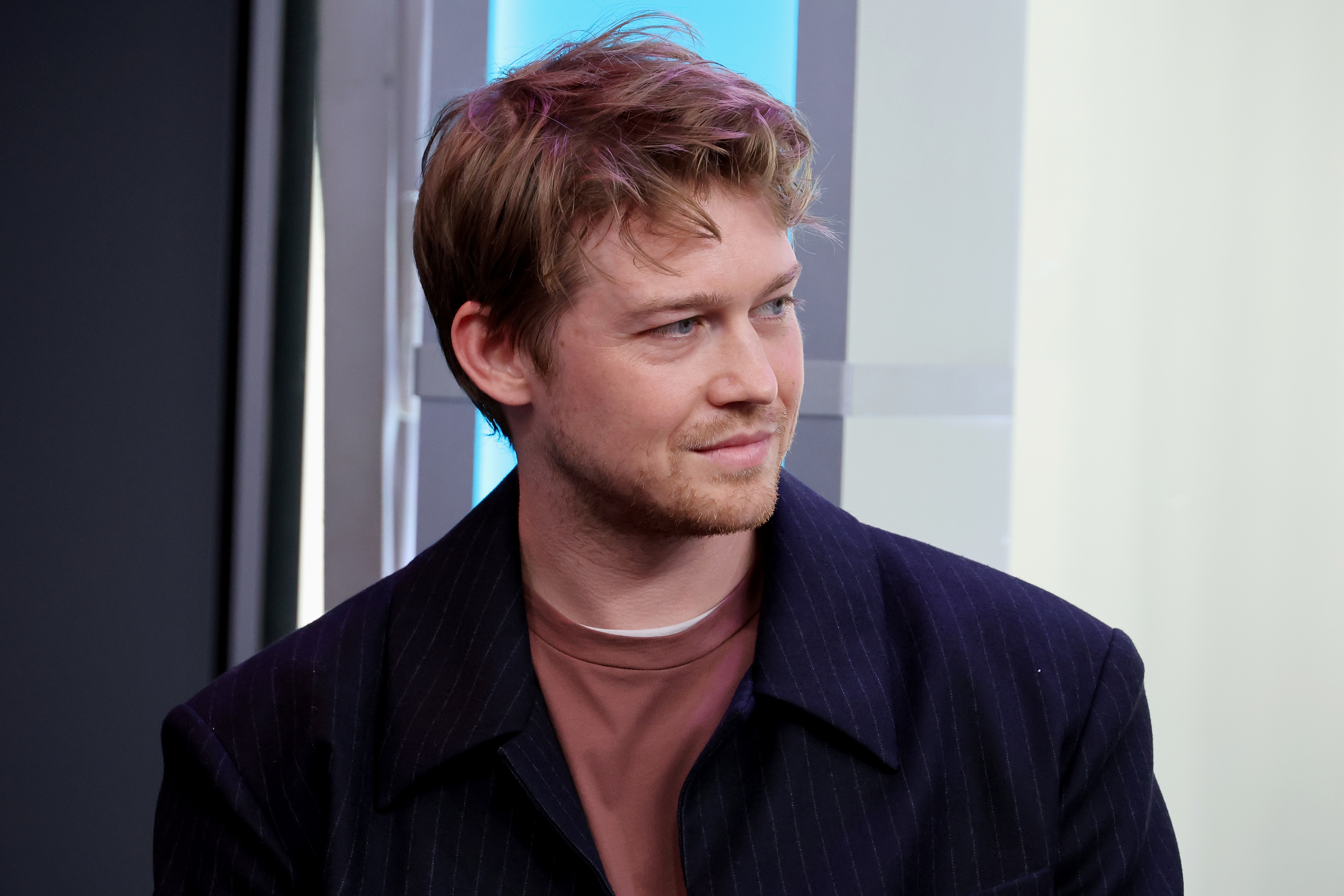 Joe Alwyn wearing a jacket and casual shirt, looking to the side