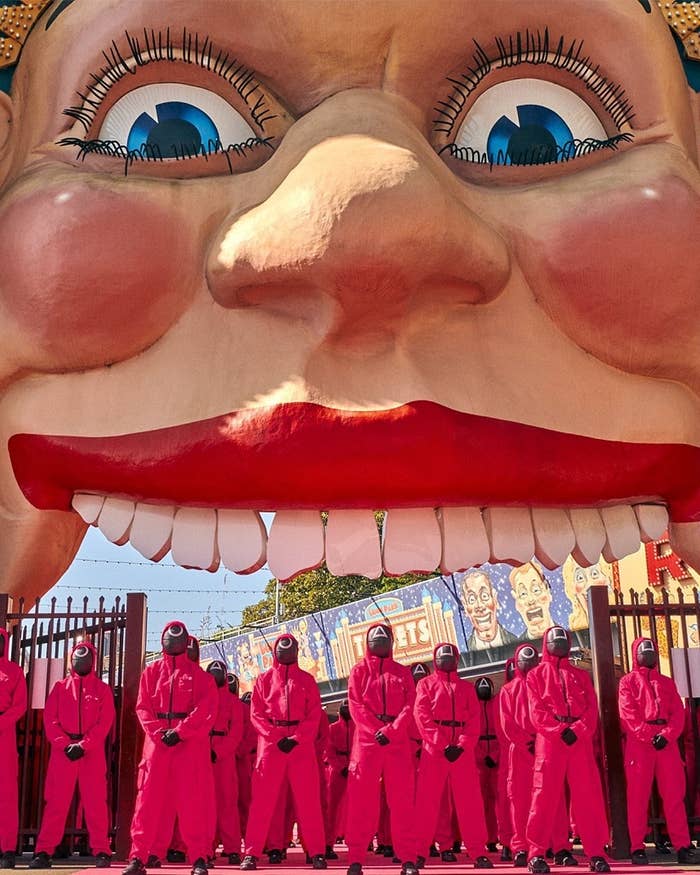 Large face sculpture at an amusement park entrance with people in matching red suits and helmets in front