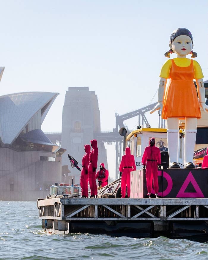 Large doll and people in pink costumes on a barge in front of the Sydney Opera House