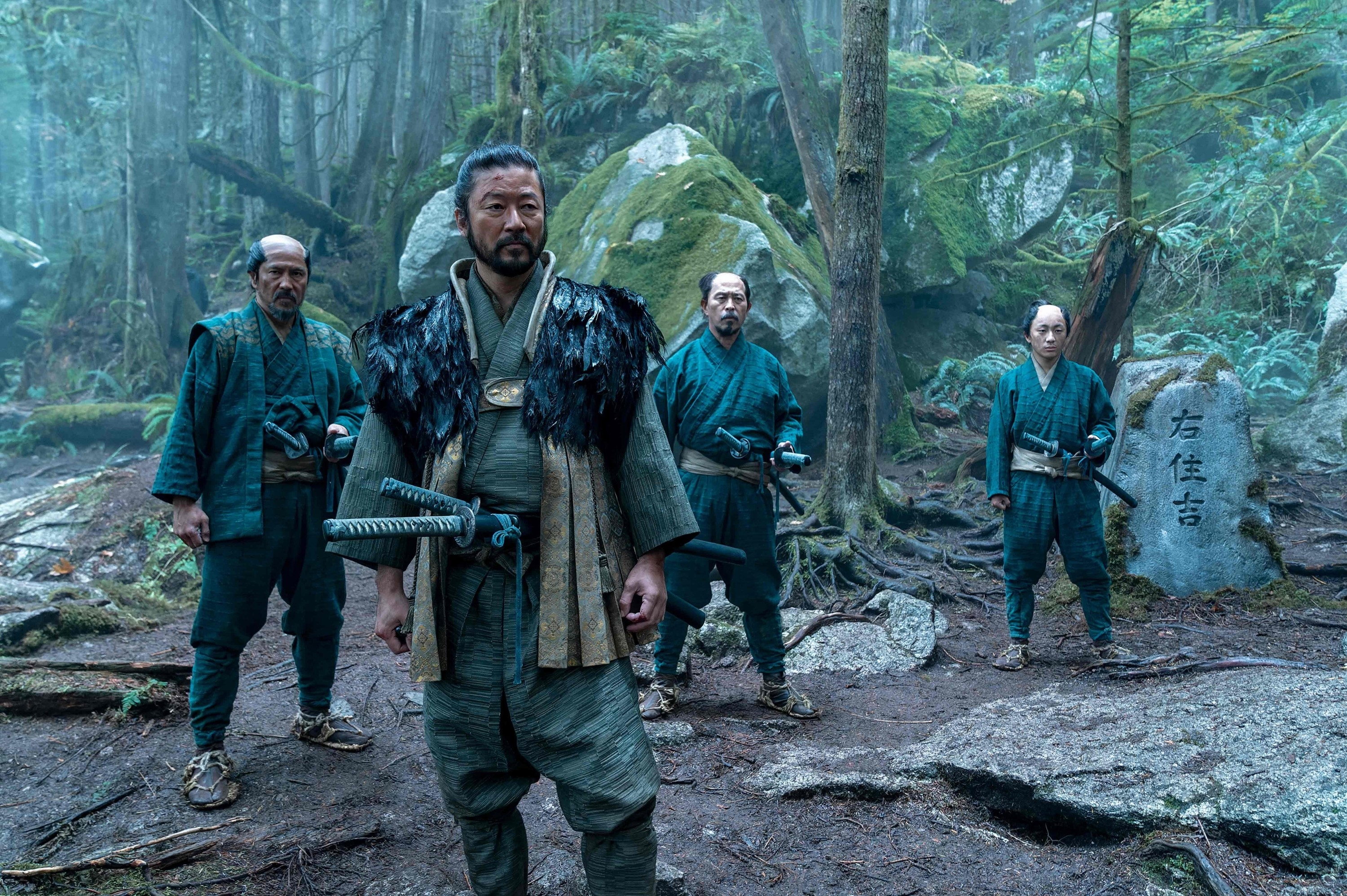 Four characters in samurai attire stand in a forest. The central figure wears a fur-trimmed robe, conveying a scene from a TV or movie setting