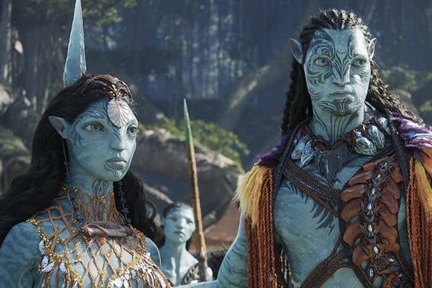 Two fictional, blue-skinned characters with intricate body designs stand in a forest setting, wearing detailed tribal attire