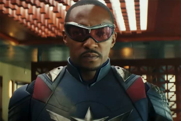 Person in futuristic suit with armor and sunglasses, standing indoors with a textured ceiling