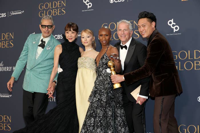 Jeff Goldblum, Michelle Yeoh, Ariana Grande, Cynthia Erivo, Marc Platt and Jon M. Chu pose with a Golden Globe award