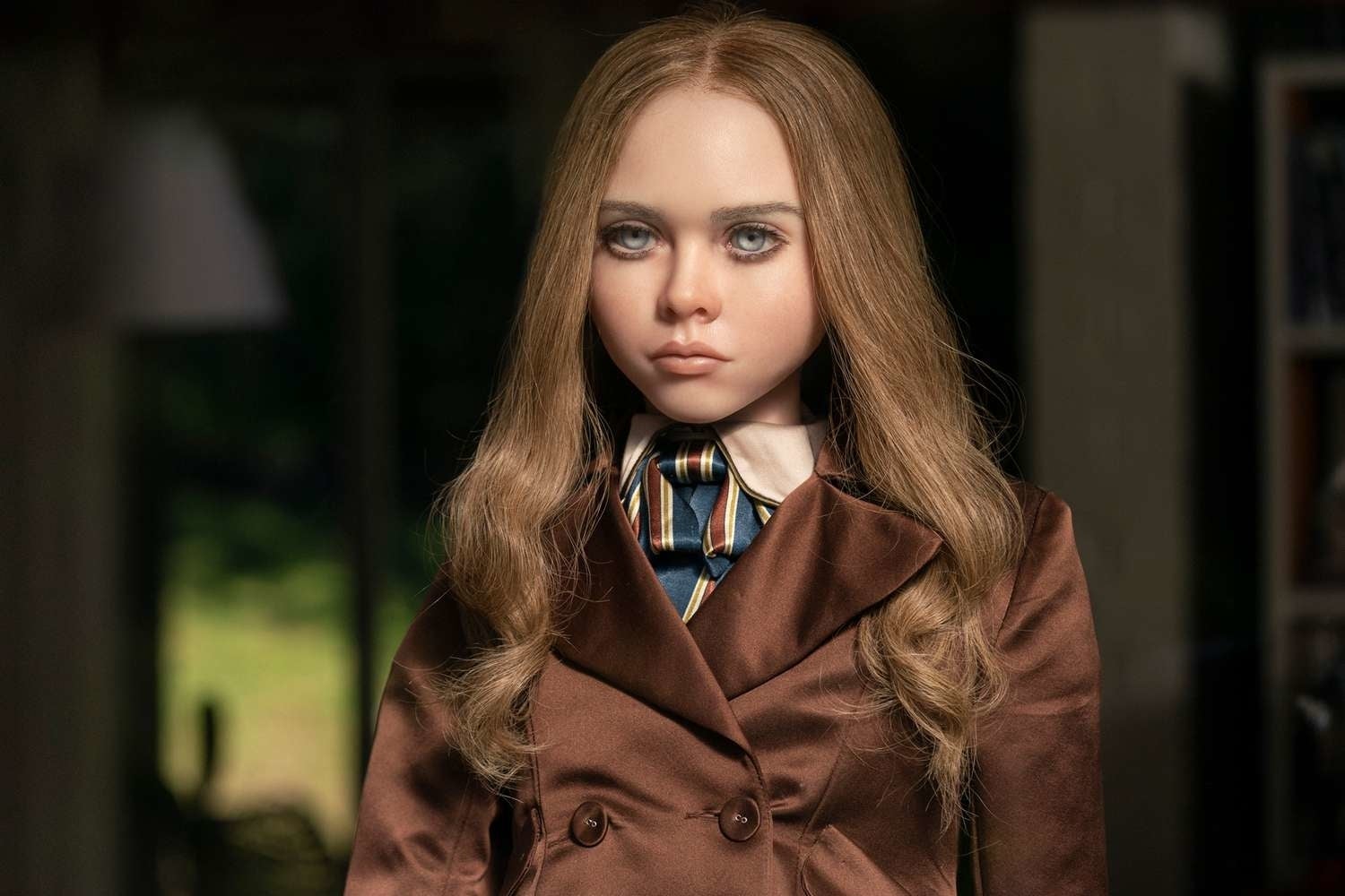 A realistic doll with long hair, wearing a brown suit and striped tie, looking forward