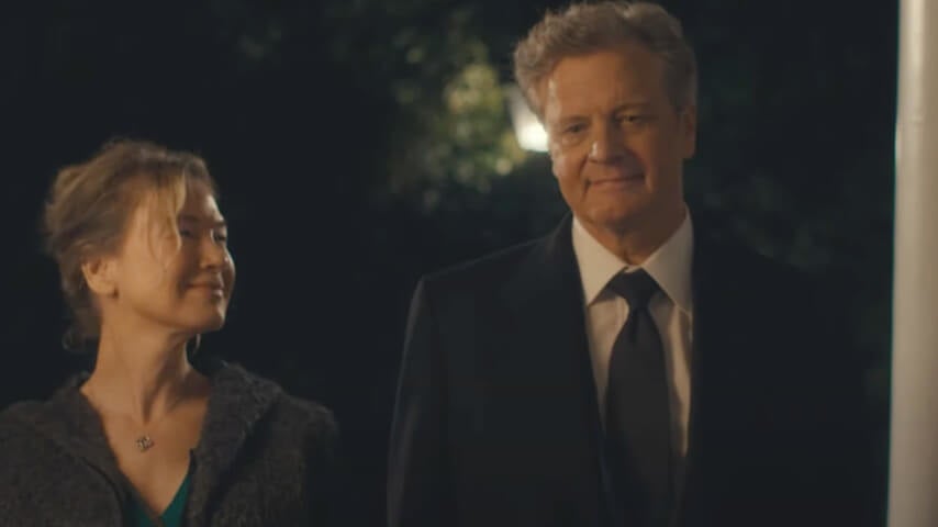 Two people in evening wear walking together outdoors at night, smiling warmly at each other