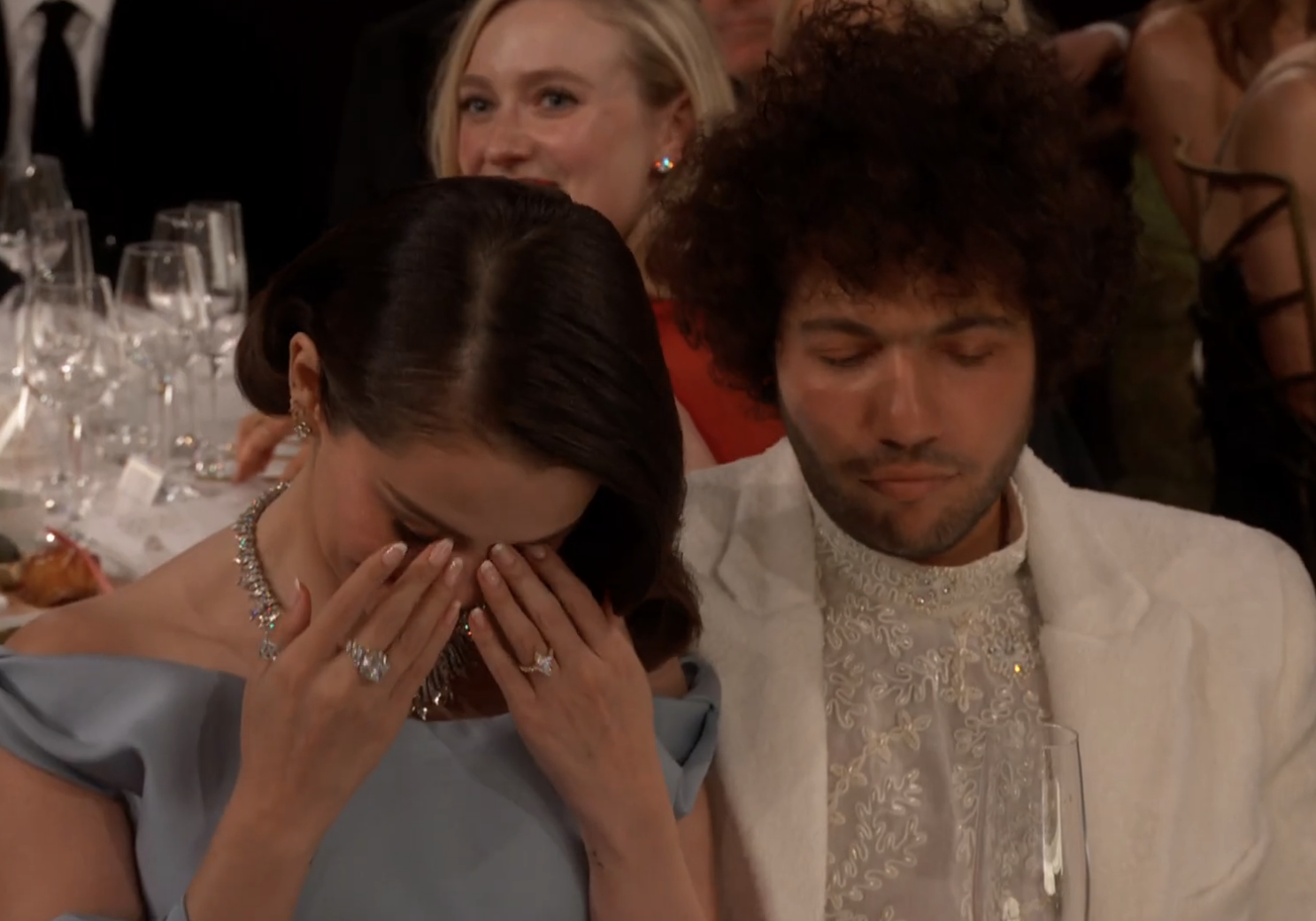 Selena Gomez looking down with her hands covering her face, next to Benny Blanco at the Golden Globes