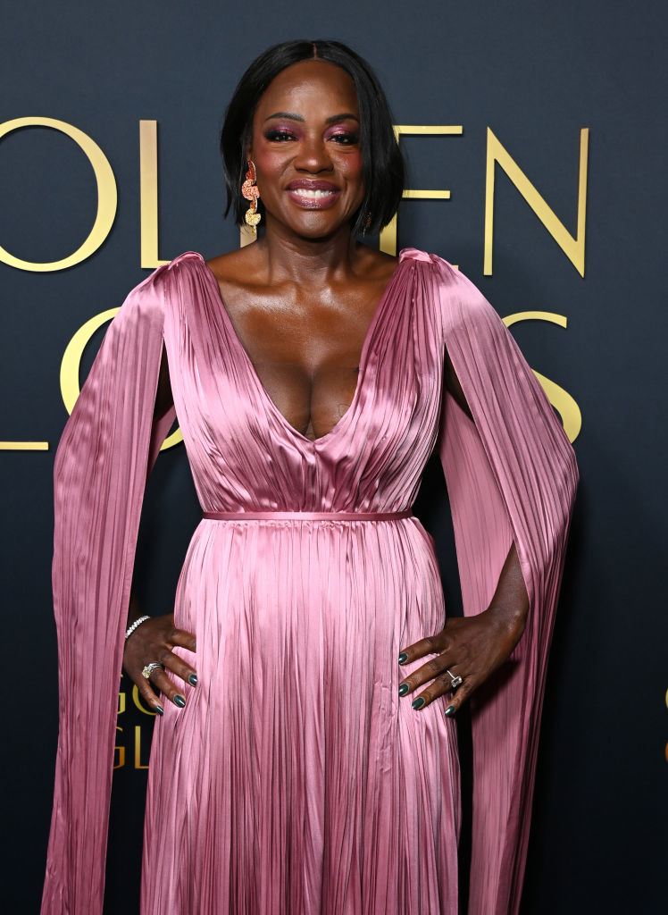Viola in an elegant, draped gown with pleated long sleeves at a formal event, smiling at the camera