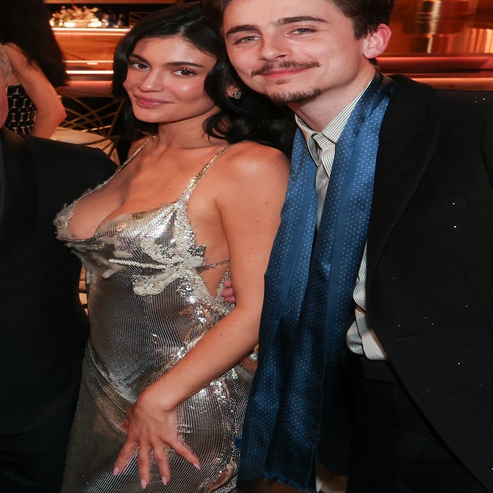 Two people posing at an event; one in a glittery dress, the other in a suit with a blue scarf
