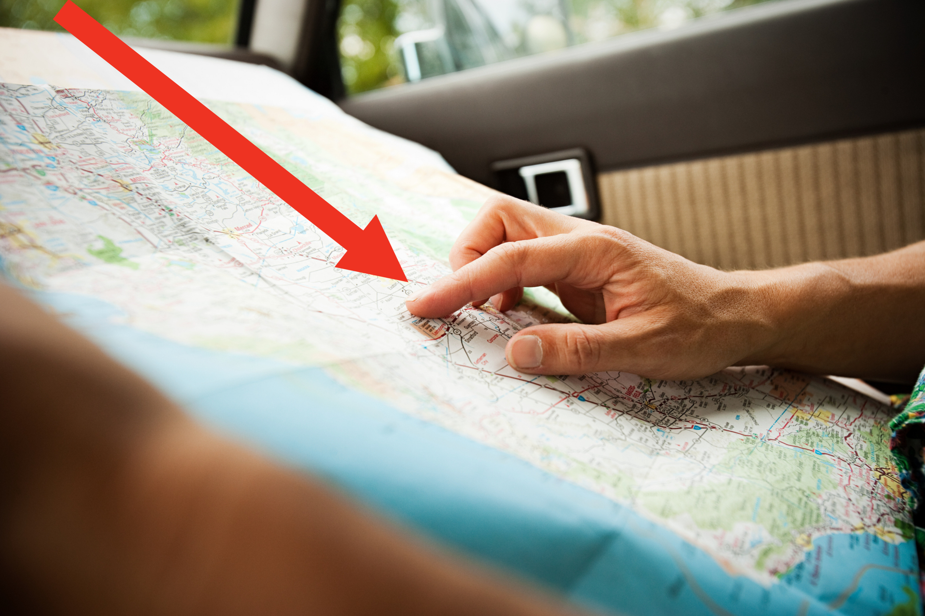 A person in a car looking at a map, pointing at a location, suggesting travel or navigation