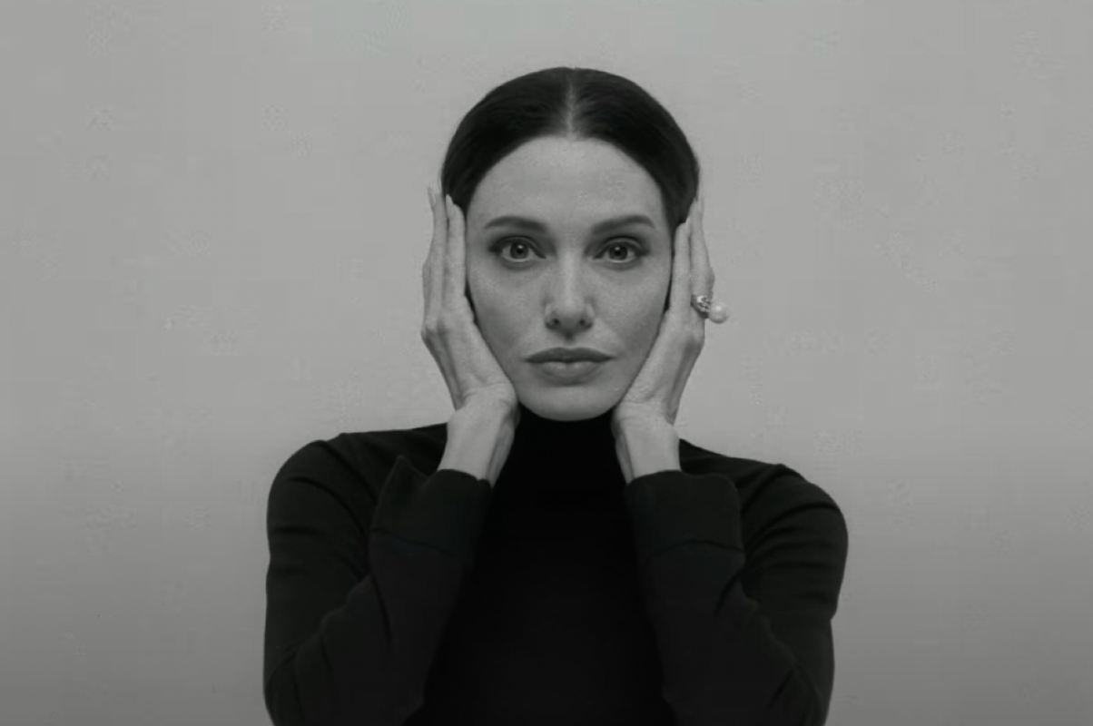 Person in a turtleneck poses with hands framing face against a plain background