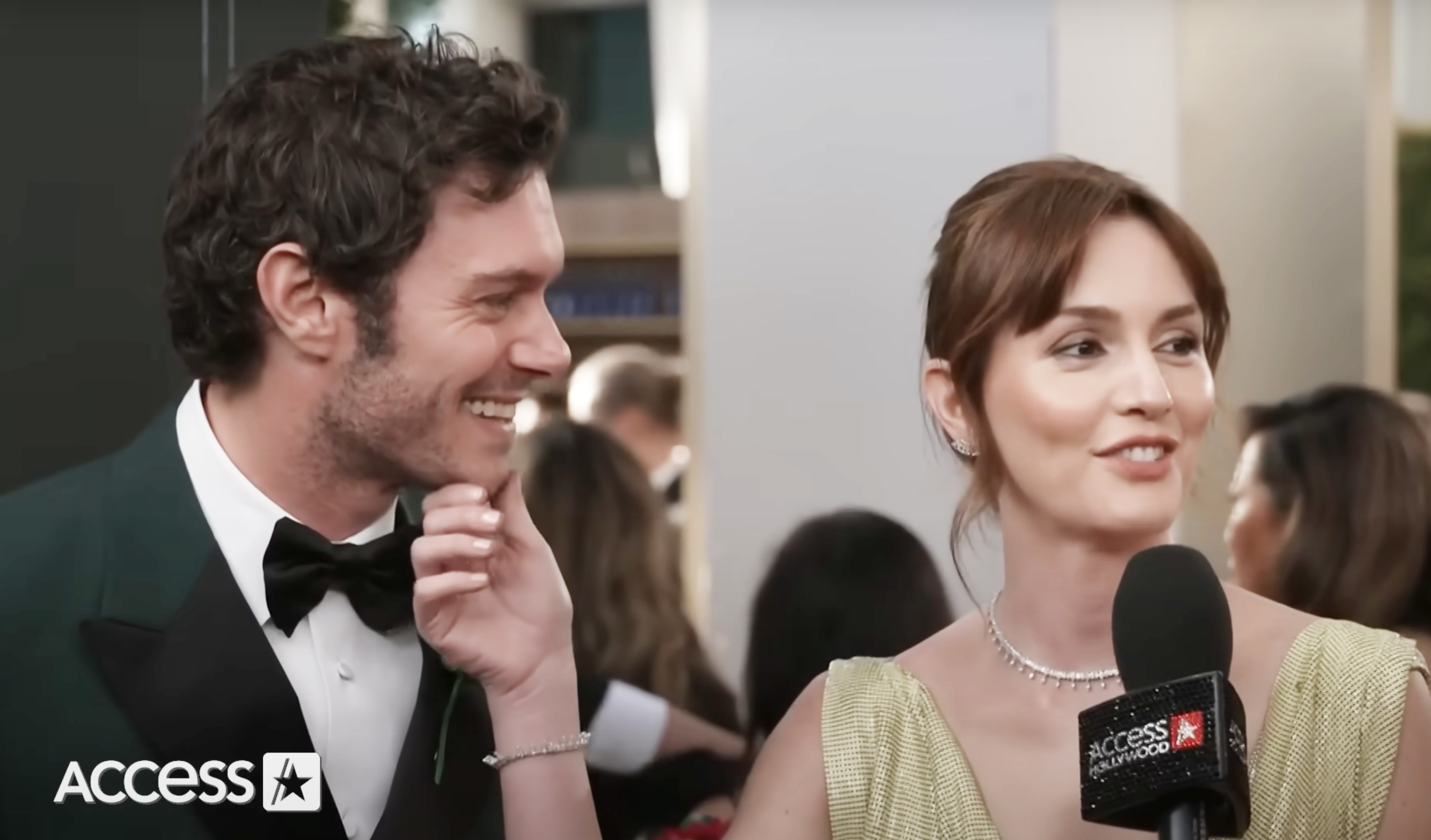 Two celebrities at a red carpet event; man in a tuxedo smiles, woman in a sleeveless gown speaks into a microphone. Access Hollywood logo visible