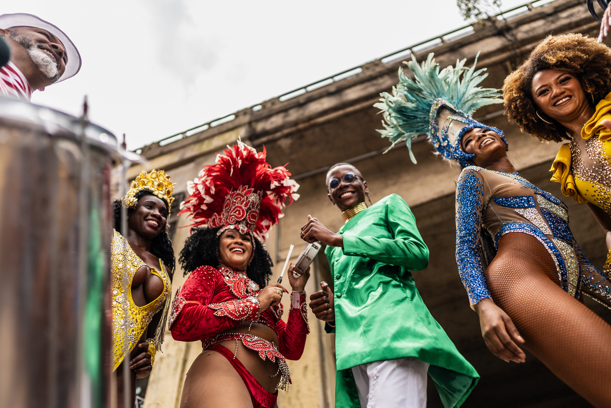 People in vibrant costumes and headdresses celebrate happily, holding musical instruments at a festive outdoor event