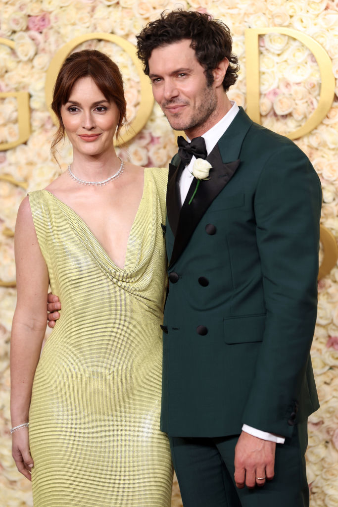 The couple on a red carpet, one in a draped, elegant gown and the other in a tailored suit with a boutonnière