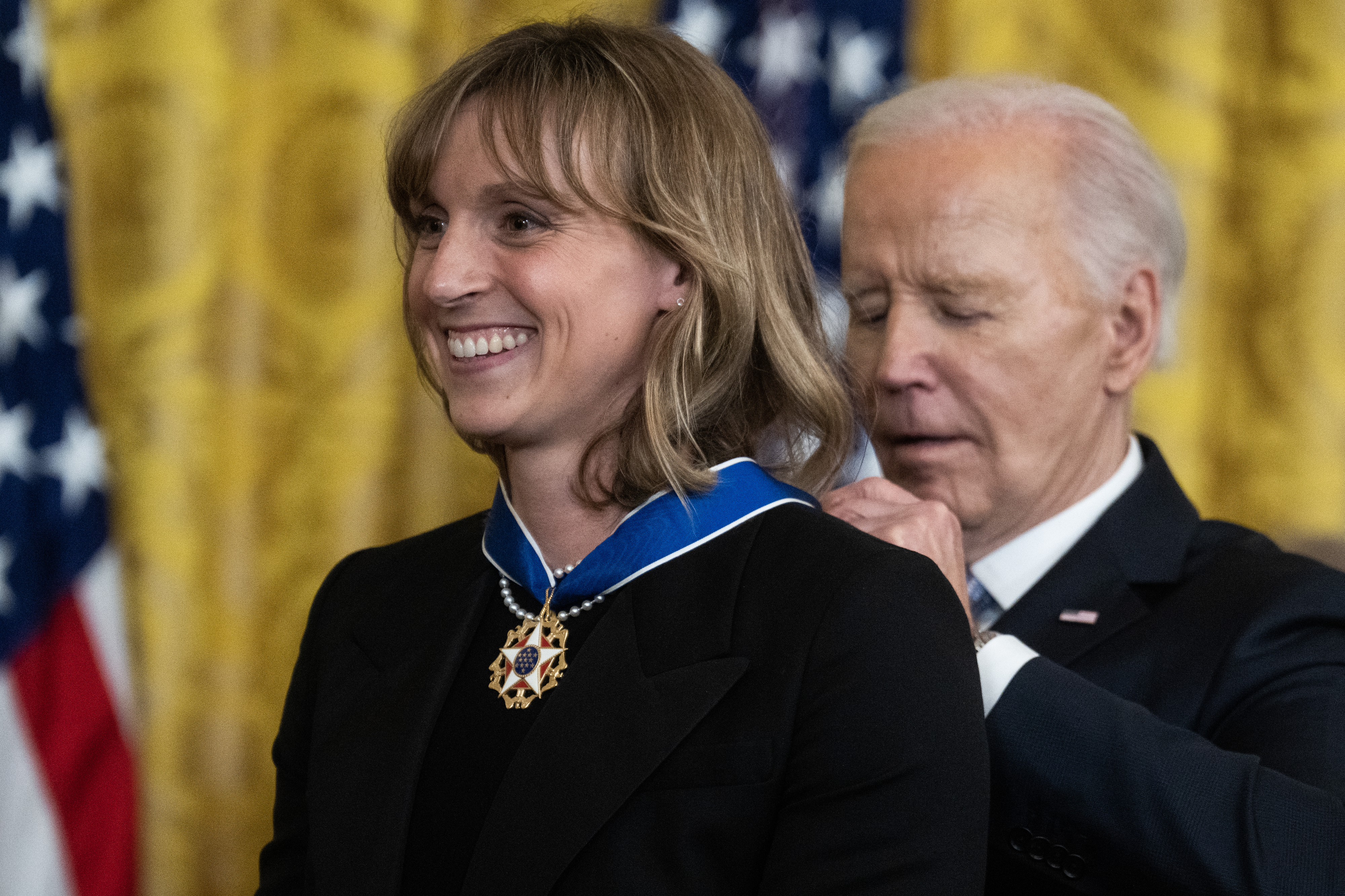 Person receiving a medal from an official in a formal setting, both smiling