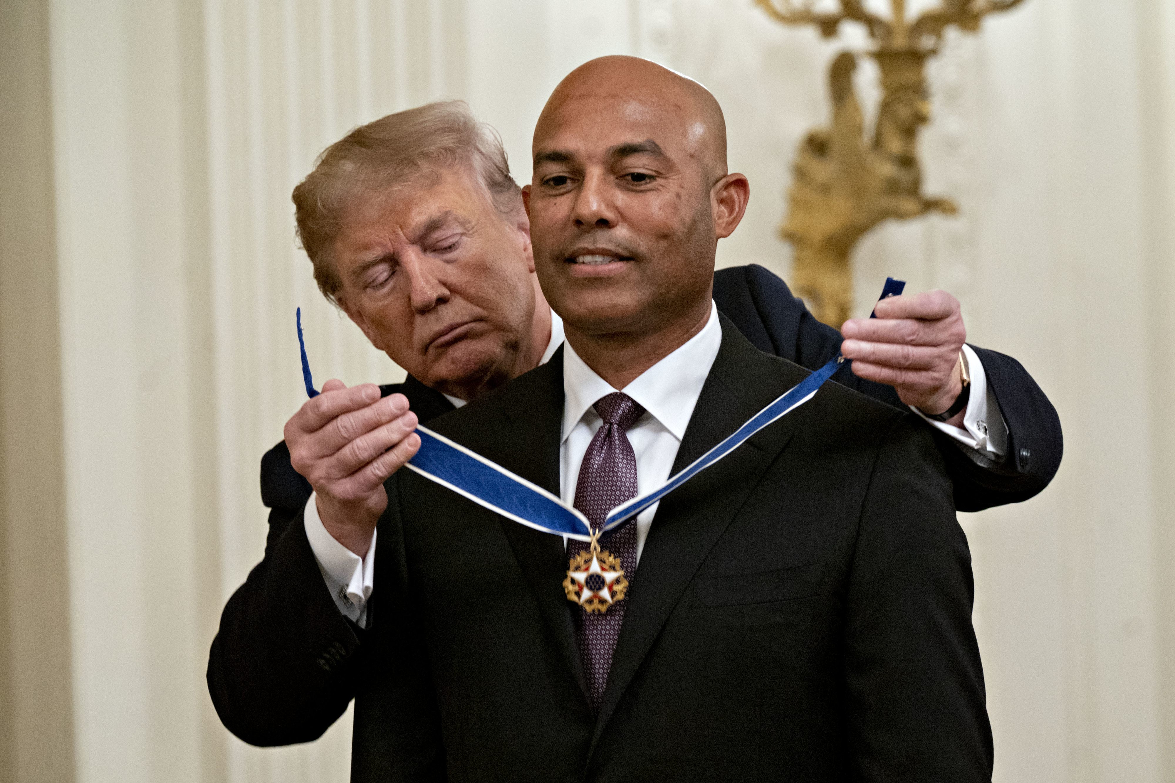 A person receives a medal on a ribbon in an official ceremony setting. The award recipient wears a suit and tie