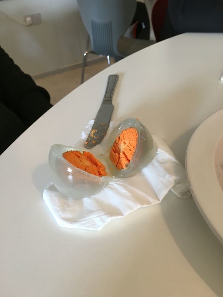 A sliced, transparent egg with an orange yolk on a napkin and a table setting, accompanied by a butter knife