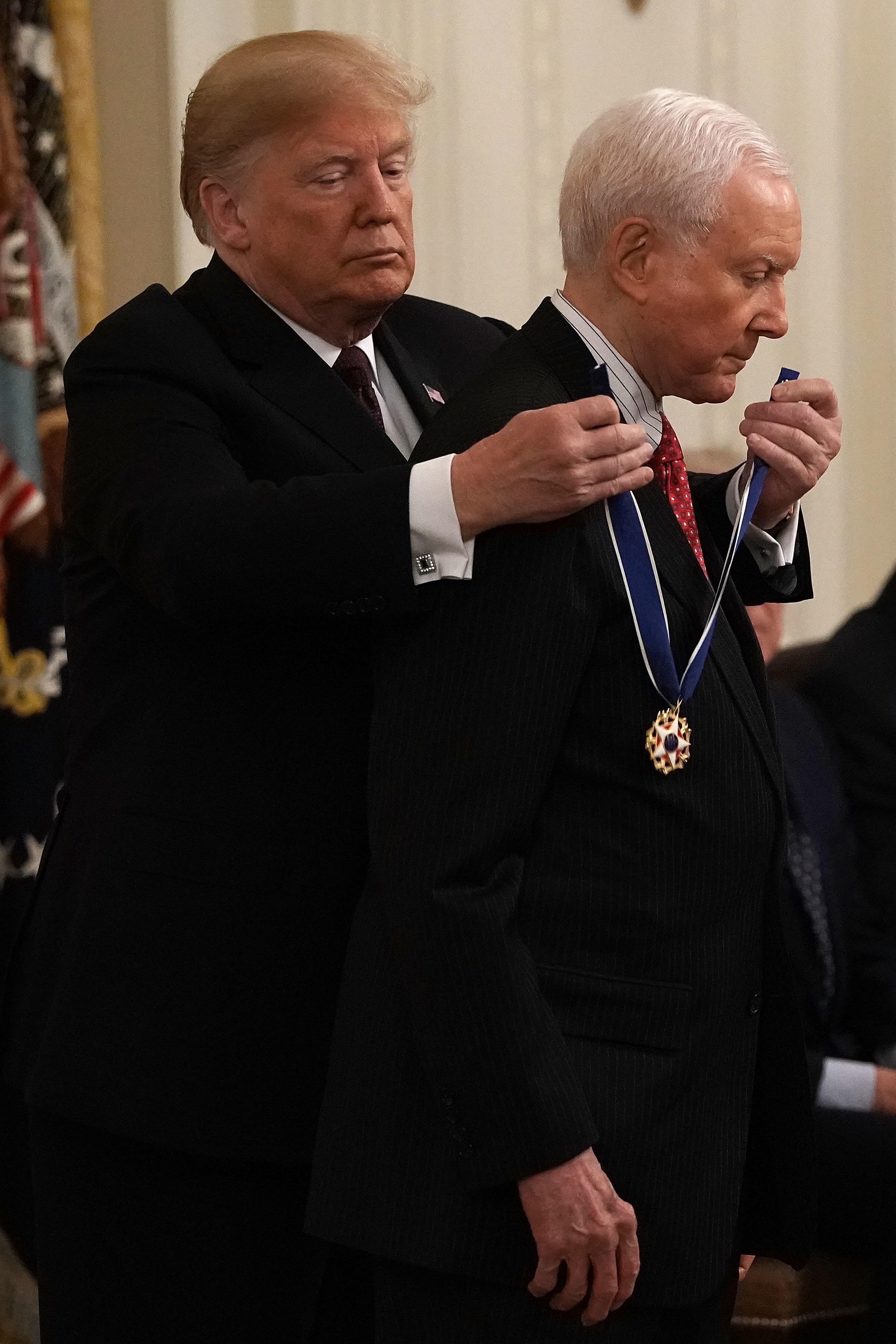 Two men in formal wear at an award ceremony; one is placing a medal on the other