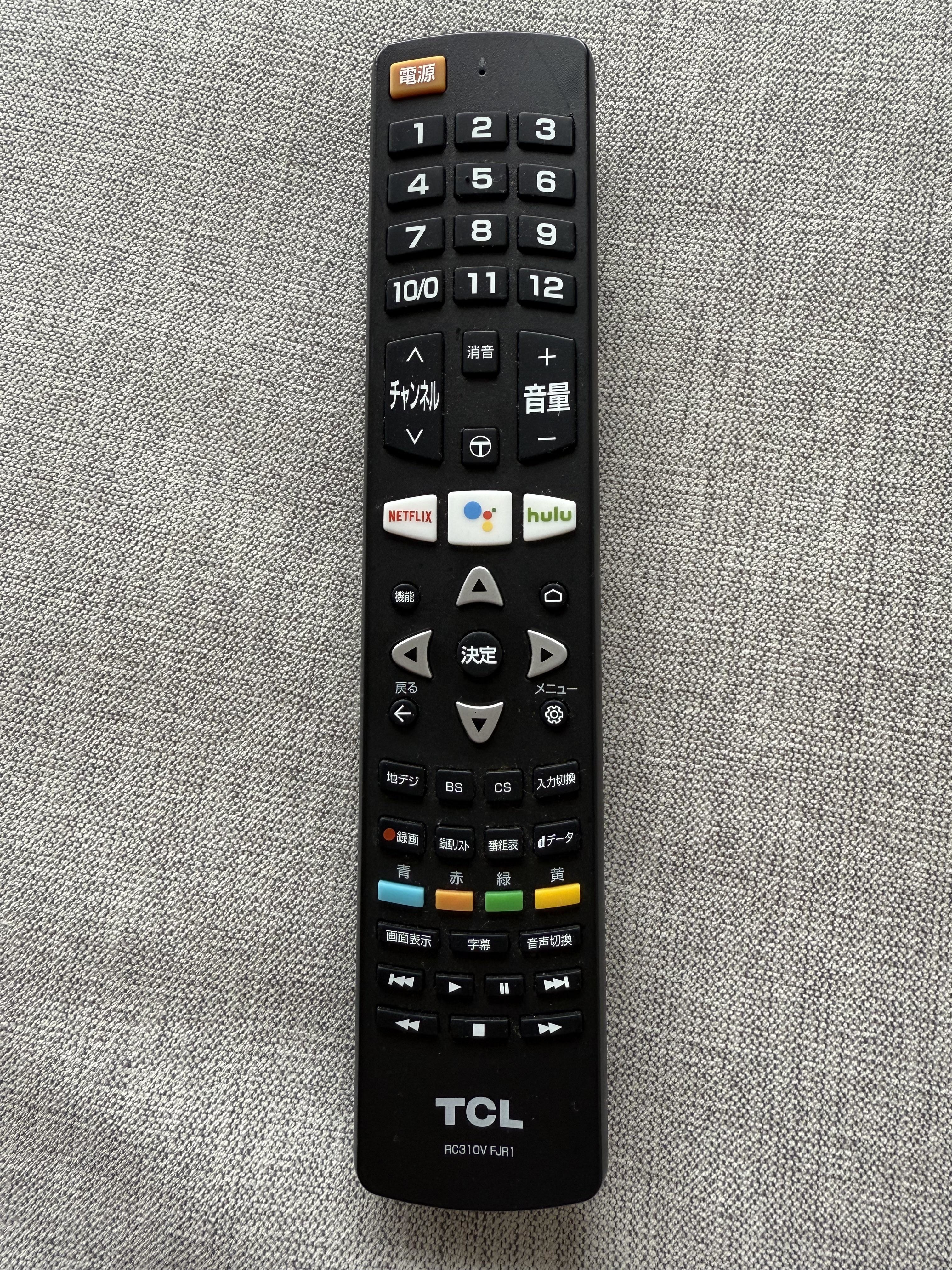 TV remote control with various streaming and navigation buttons, including Netflix, Hulu, and directional arrows, on a fabric surface