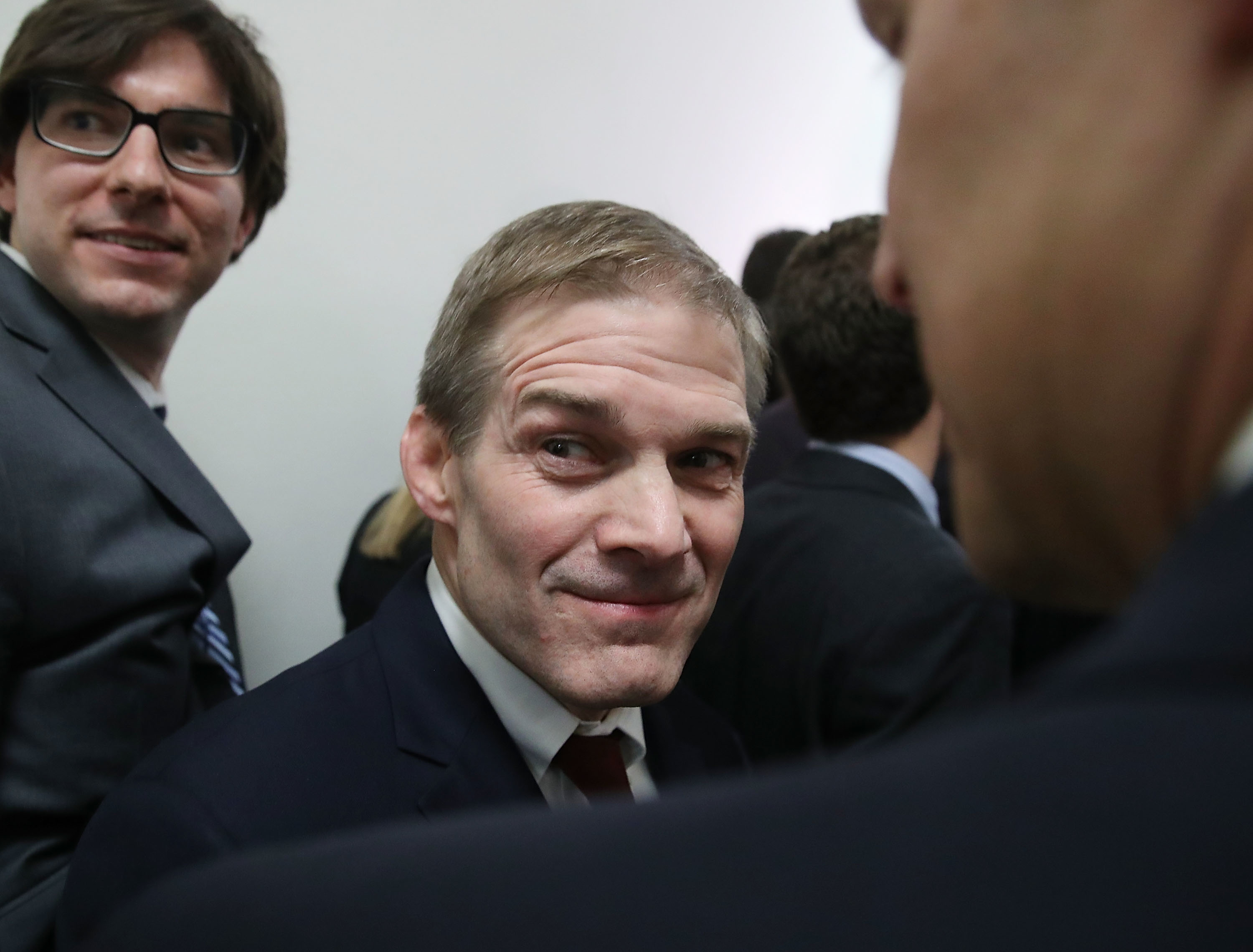 A man in a suit with a slight smile stands among others at a crowded event