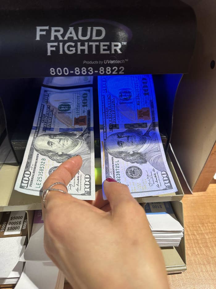 Hands using a fraud detection machine to check the authenticity of hundred-dollar bills