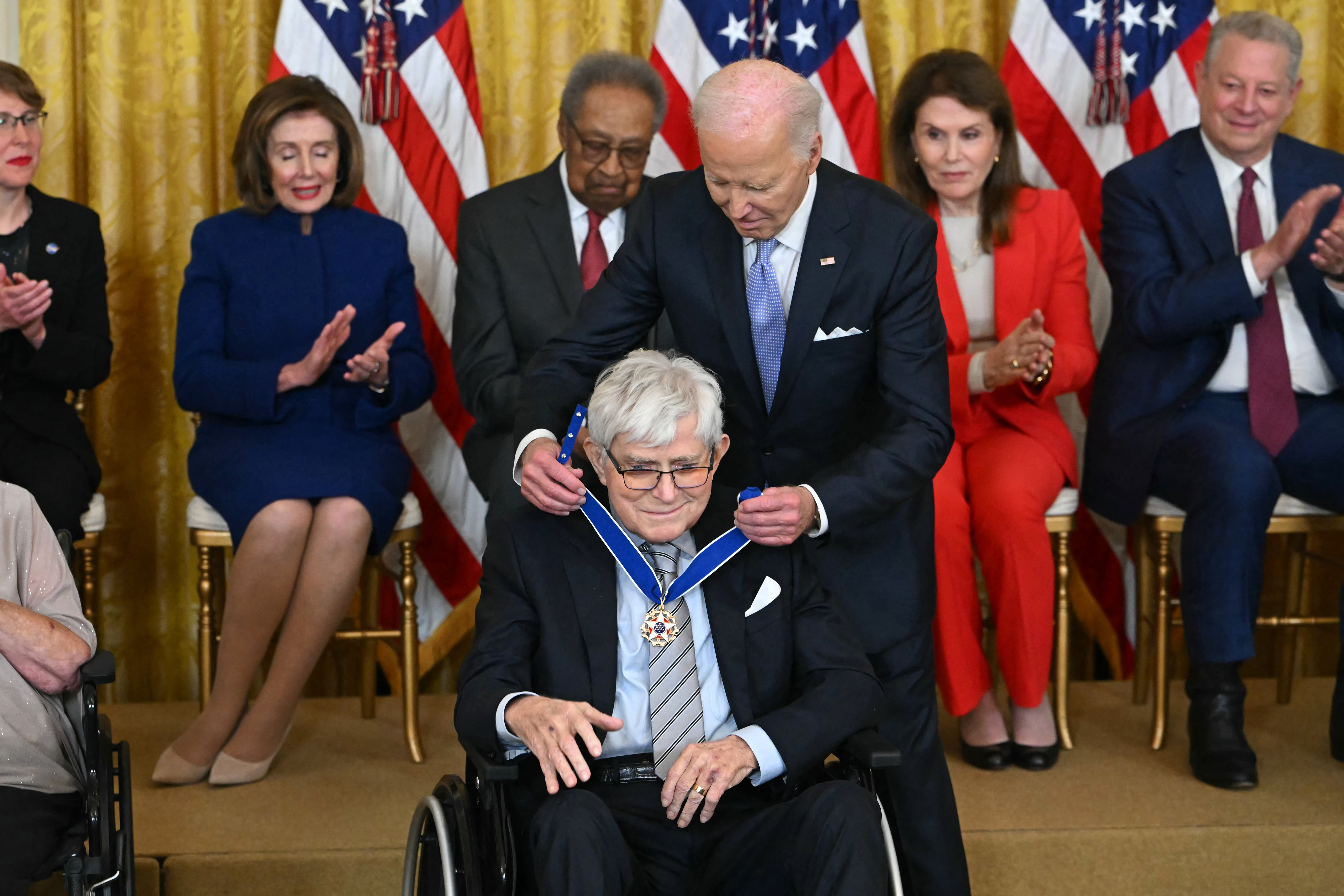 President awards a medal to an elderly man in a ceremony, with officials applauding in the background