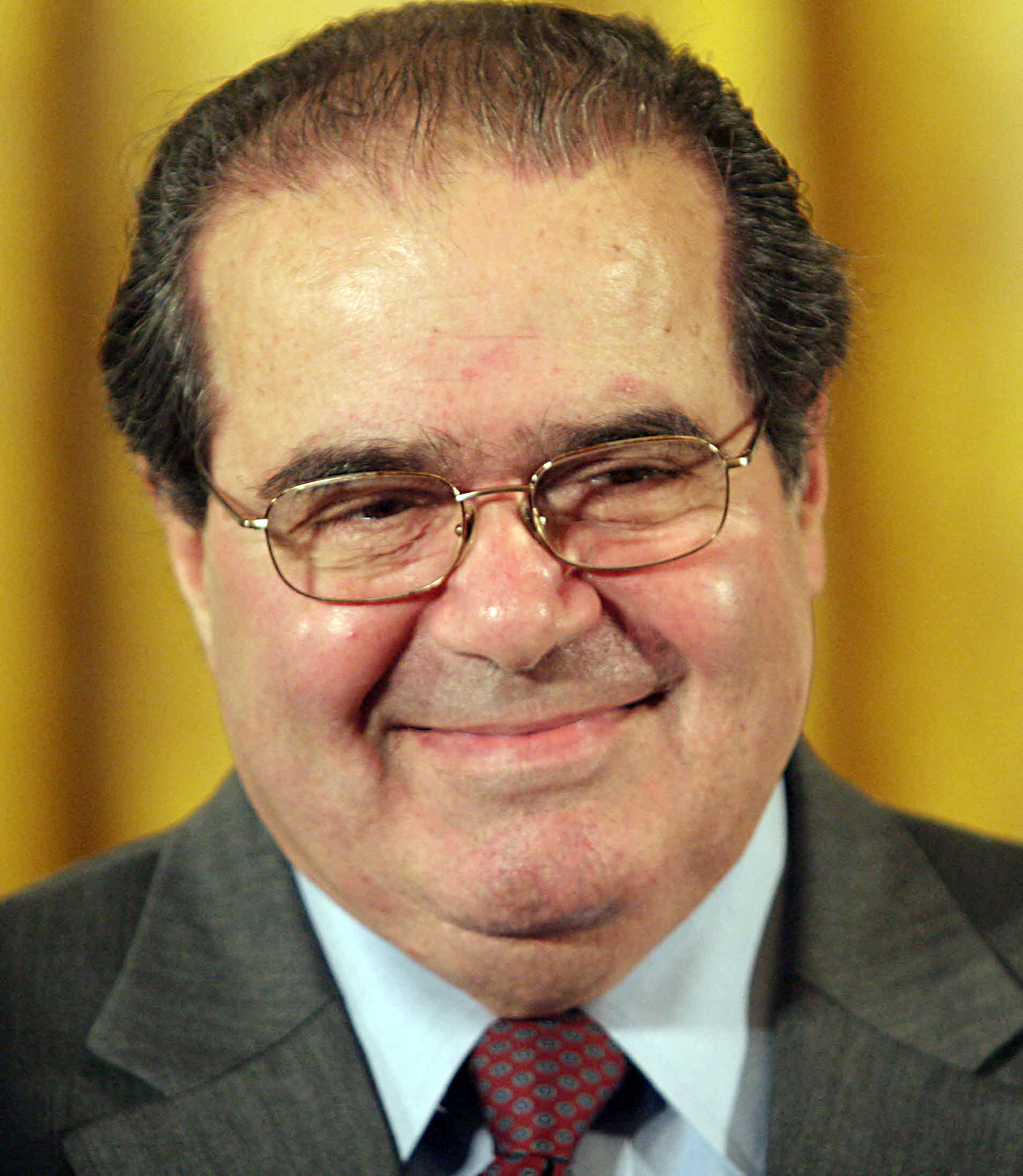 A man in a suit and tie smiling, wearing glasses