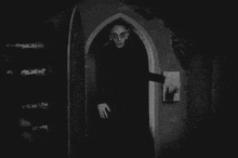 Escena clásica de una figura vampírica saliendo de una puerta arqueada en una película de terror en blanco y negro