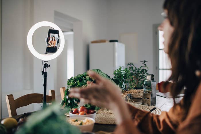 Person recording a cooking video at a kitchen table with fresh ingredients and a ring light