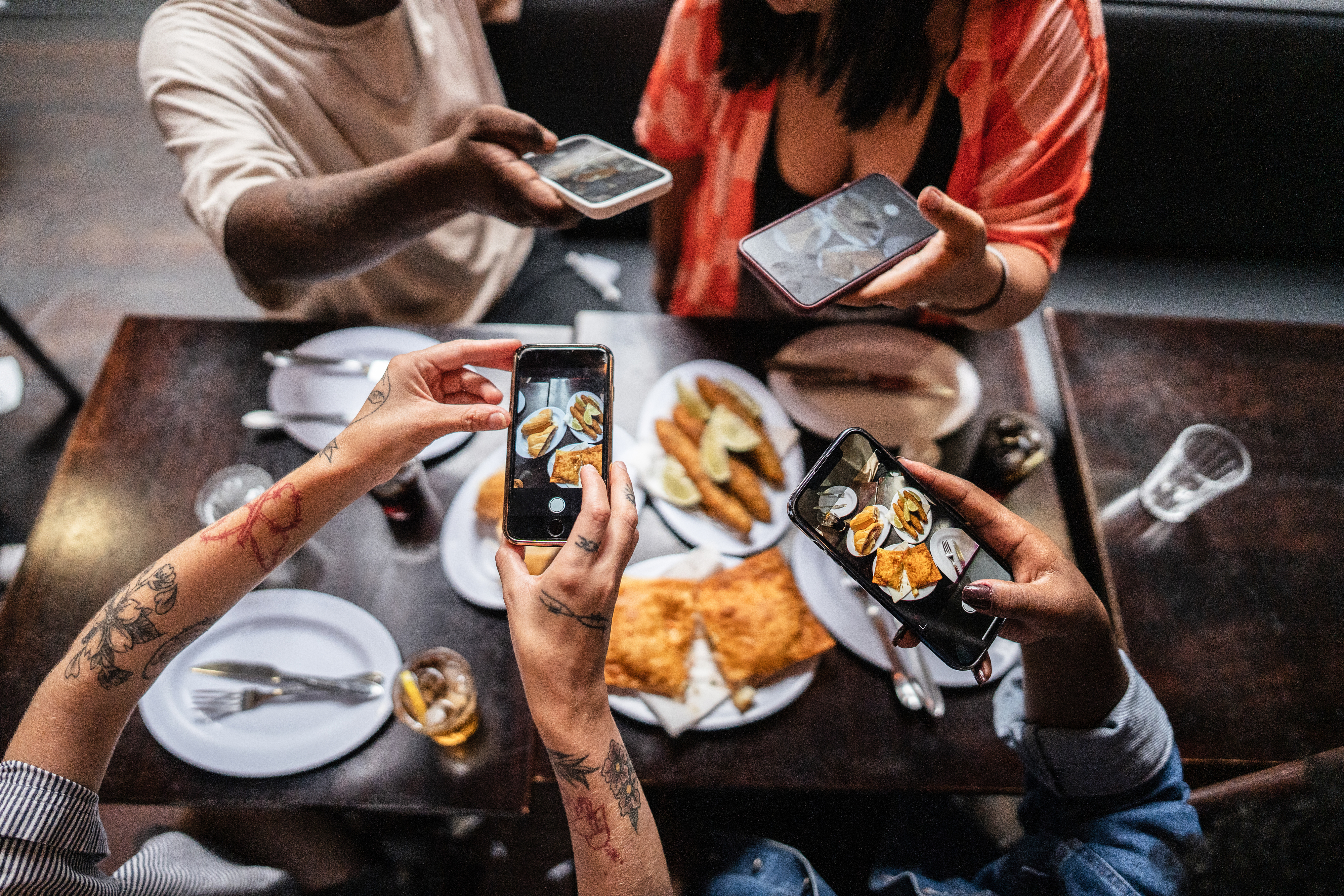 People taking photos of a meal at a restaurant, capturing dishes such as empanadas and garnished appetizers on white plates