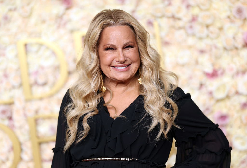 Person in elegant black dress smiles in front of a floral backdrop, attending a celebrity event