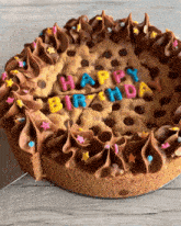 Galleta grande de cumpleaños decorada con letras de colores que dicen &quot;HAPPY BIRTHDAY&quot; y crema de chocolate con estrellas pequeñas