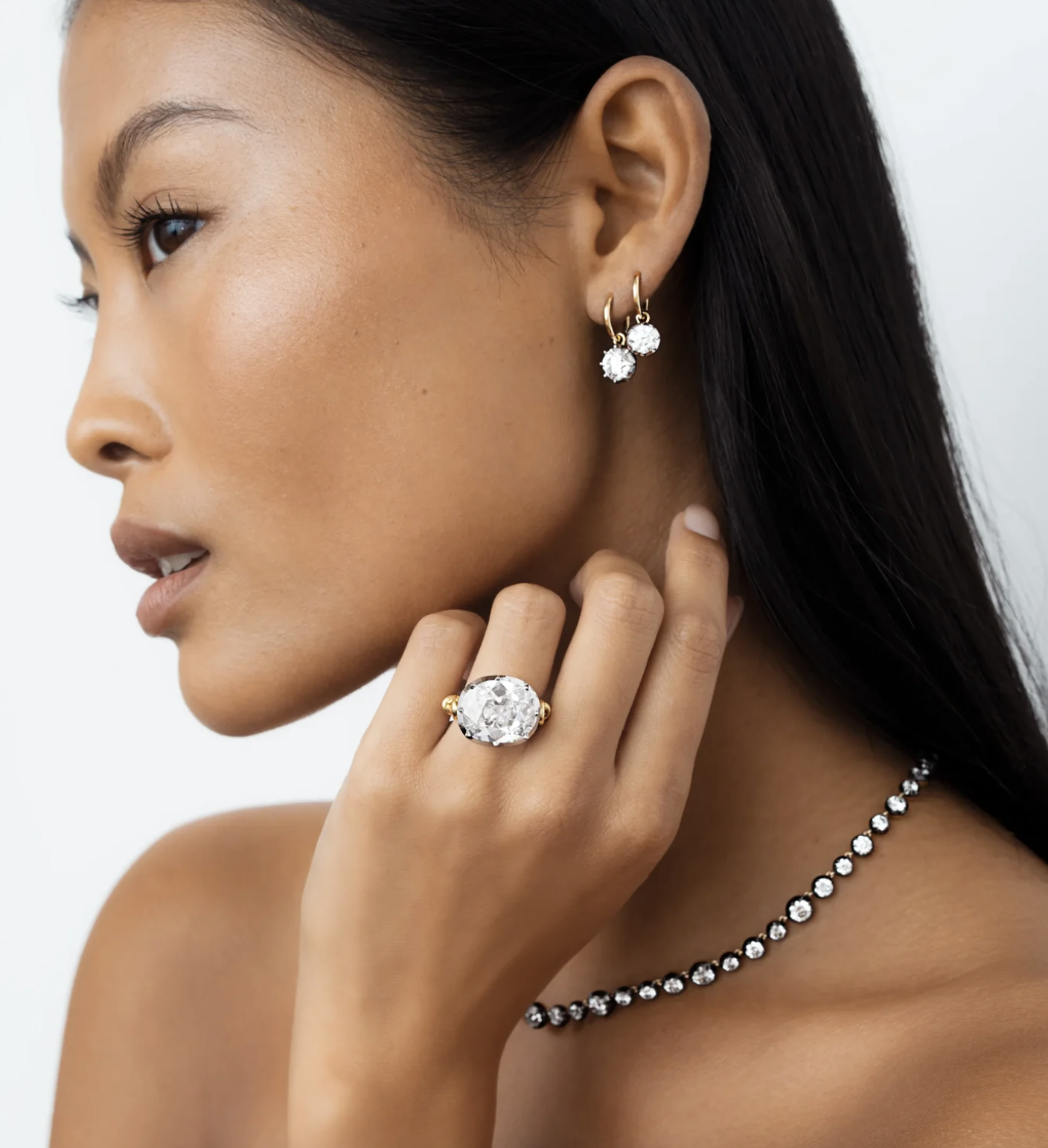 Mujer con elegante collar de gemas, pendientes y anillo brillantes. Lleva el cabello suelto y posa de perfil con una expresión serena