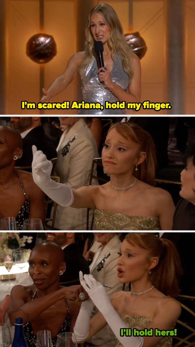 A woman in a glittery dress speaks at a formal event; two women at a table react humorously, one offering to hold the other&#x27;s finger