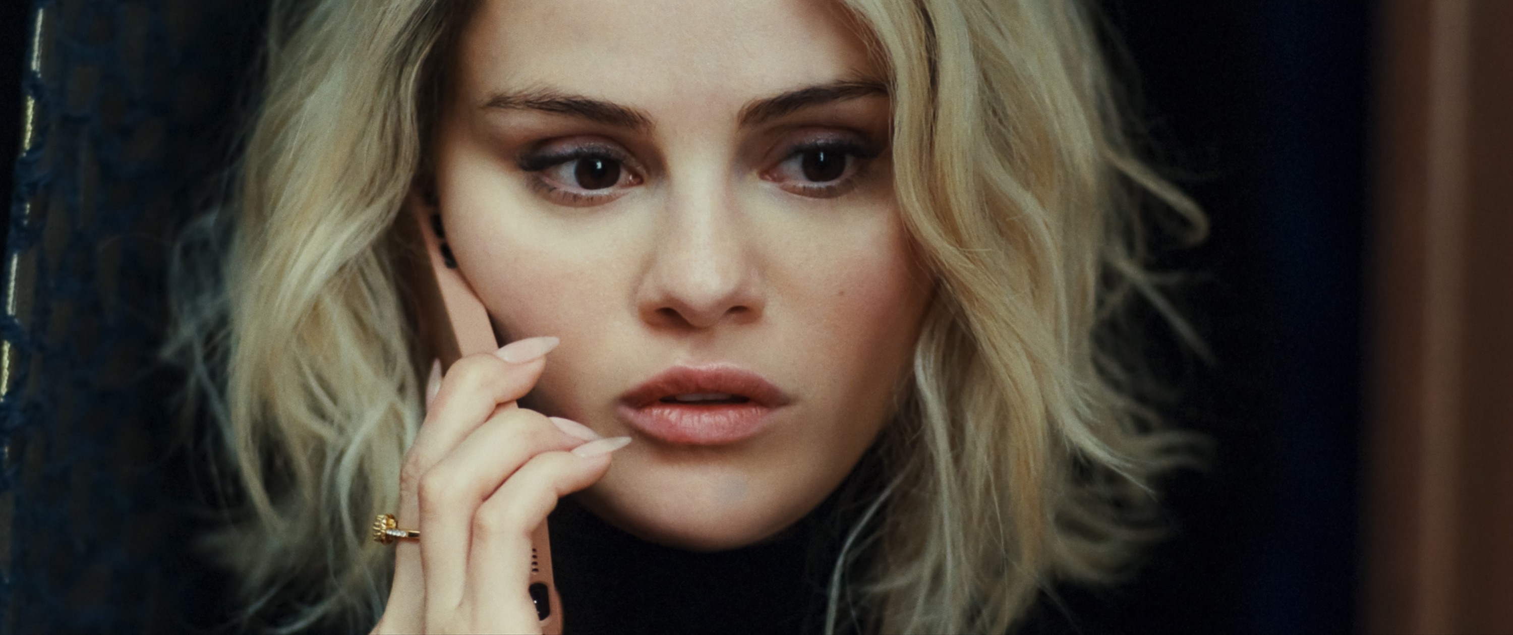 Woman with blonde hair holding a phone to her ear, looking intently, wearing a black top