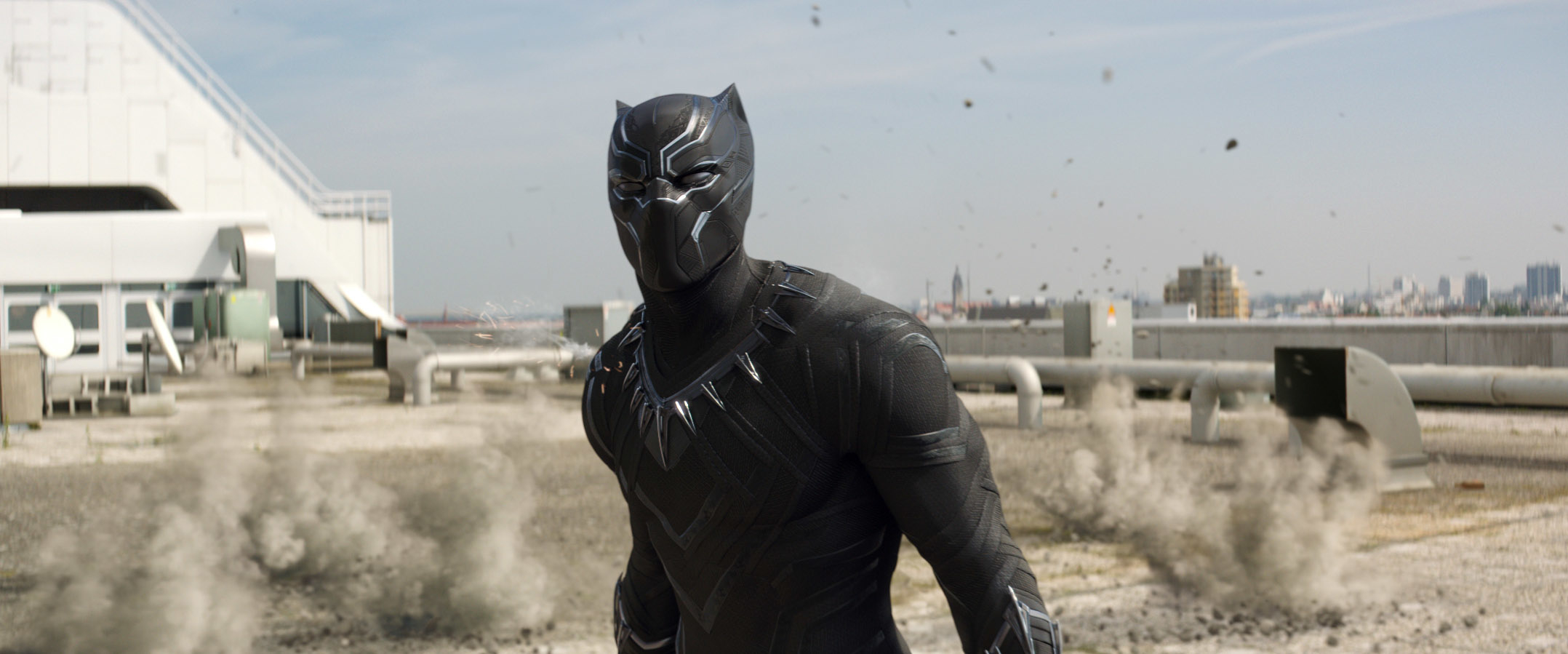 Character in a black panther costume stands on a rooftop with debris in the background