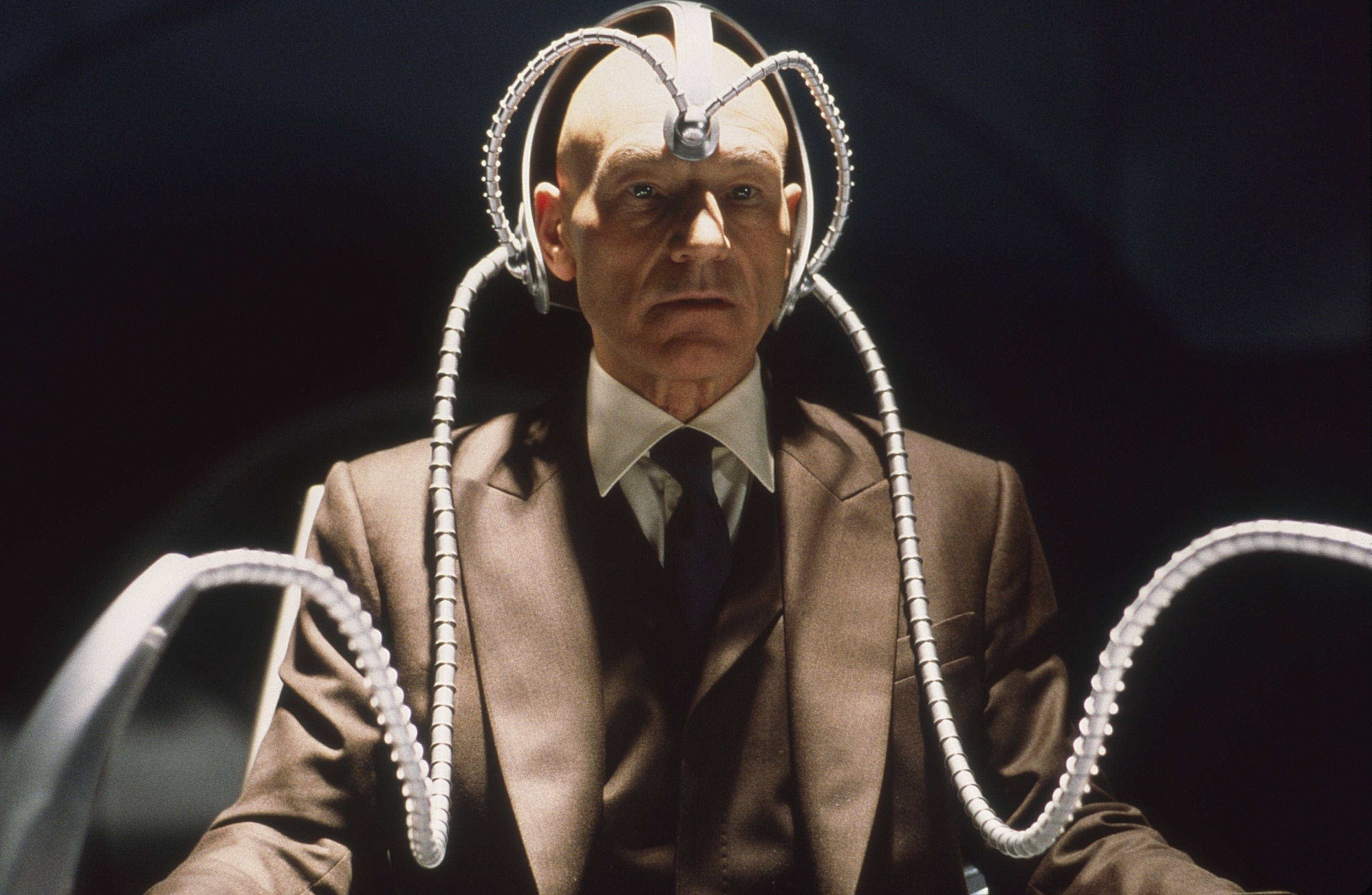 Man in a suit wearing a metallic headpiece with cables extending outward, in a sci-fi setting