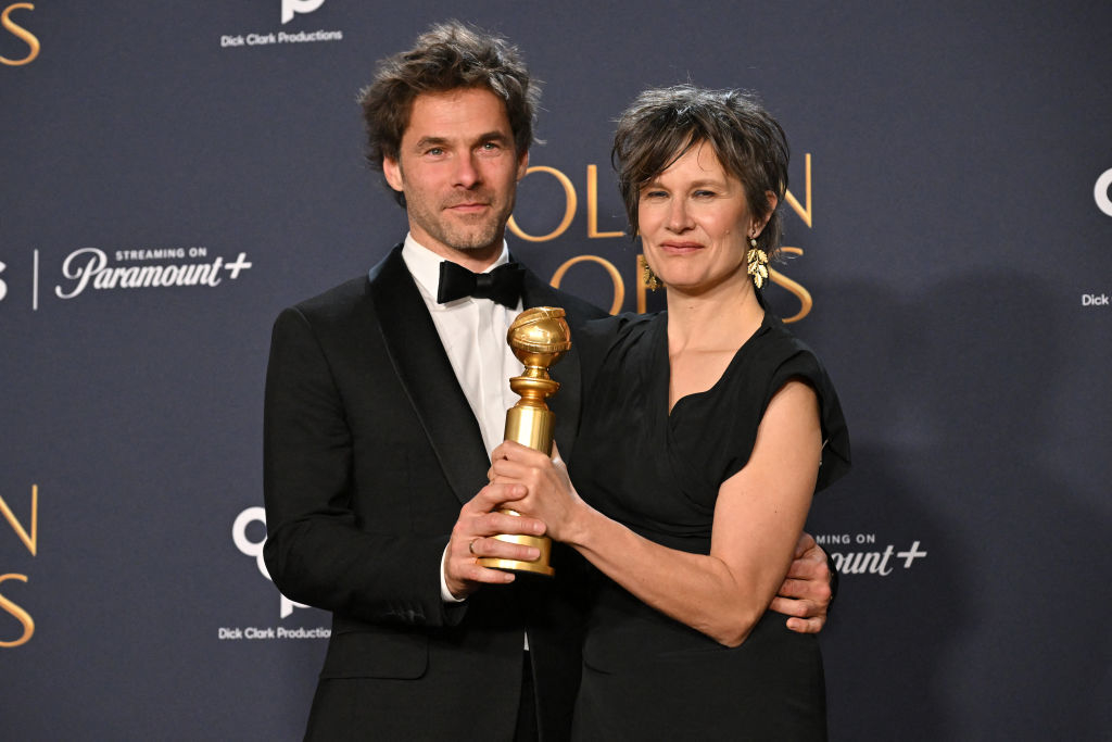 Two people in formal attire smile while holding a Golden Globe award at an event