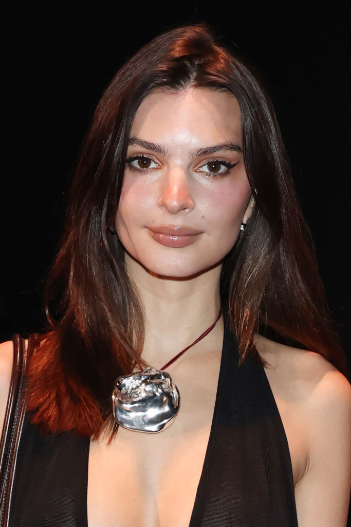 Person in sleek black halter-style dress with metallic necklace, standing against a dark background