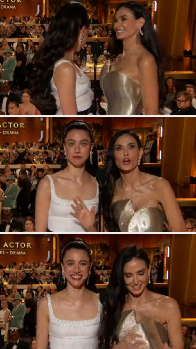 Two women on a red carpet, one in a strapless metallic gown and the other in a white dress, smile and pose for photos at an event