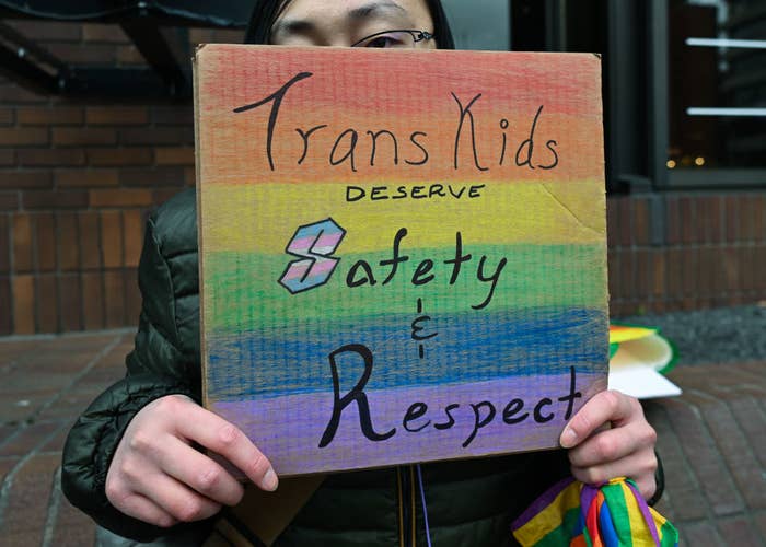 Person holding a sign reading &quot;Trans Kids Deserve Safety &amp;amp; Respect&quot;