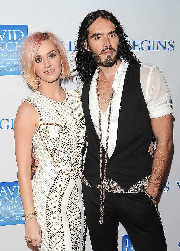 Two people posing at an event; one in a studded white dress, the other in a black vest over a white shirt