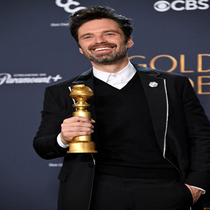 Sebastian Stan in a suit holds a Golden Globe award at an event