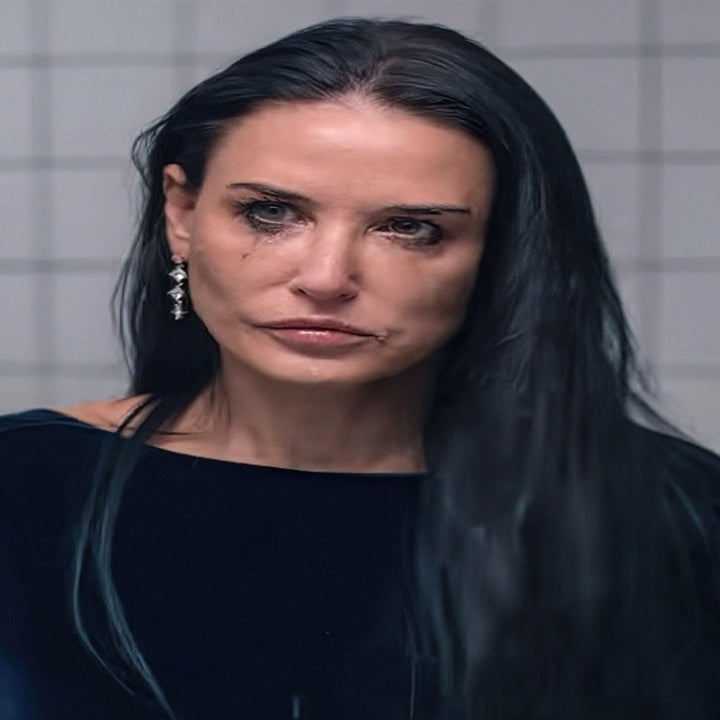 Demi with long dark hair stands in front of a tiled wall, wearing a velvet top, with a pensive expression on her face