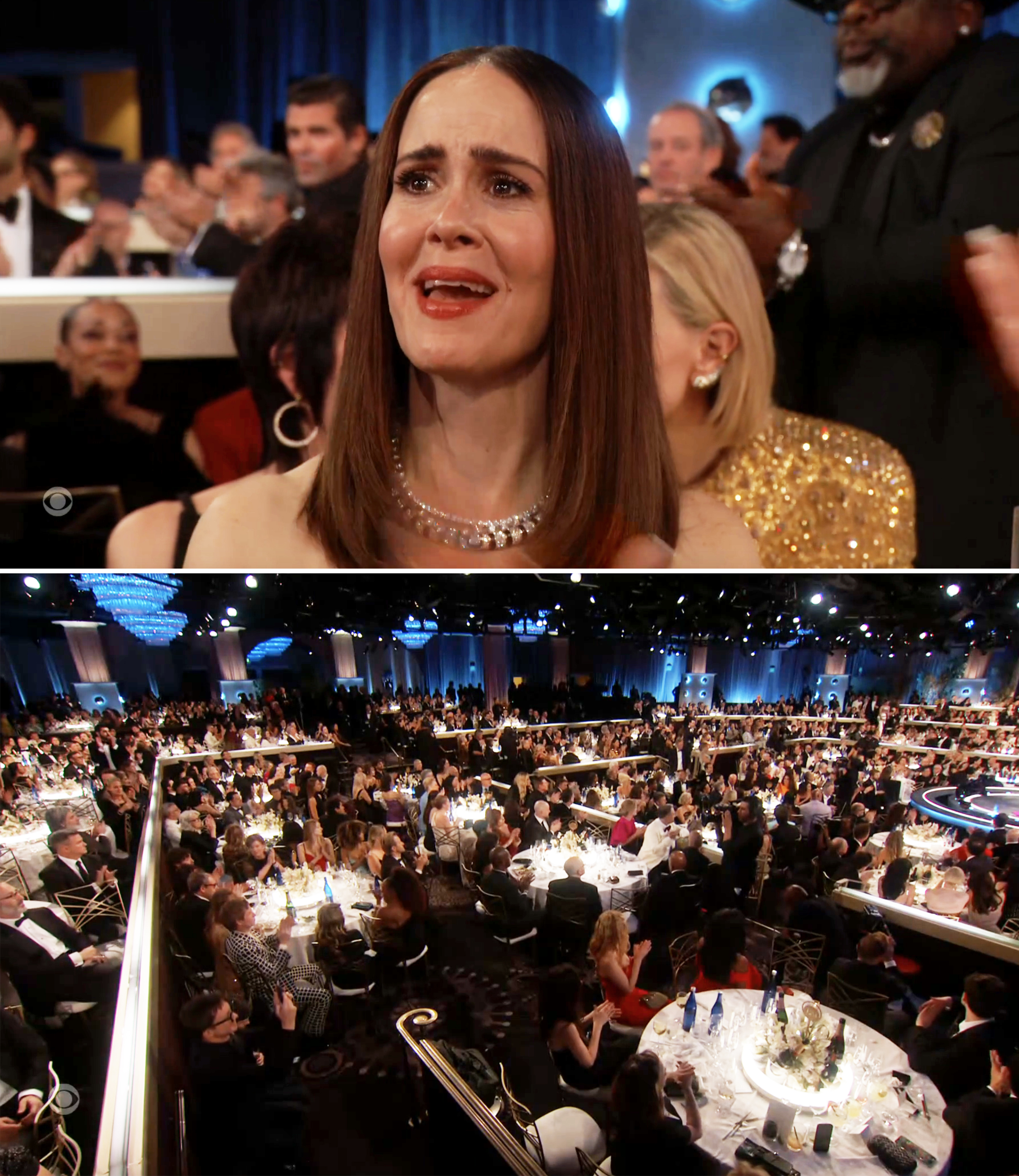 Celebrity at award show reacting emotionally; elegant, sleeveless evening dress. Audience seated at round tables in a large, decorated venue