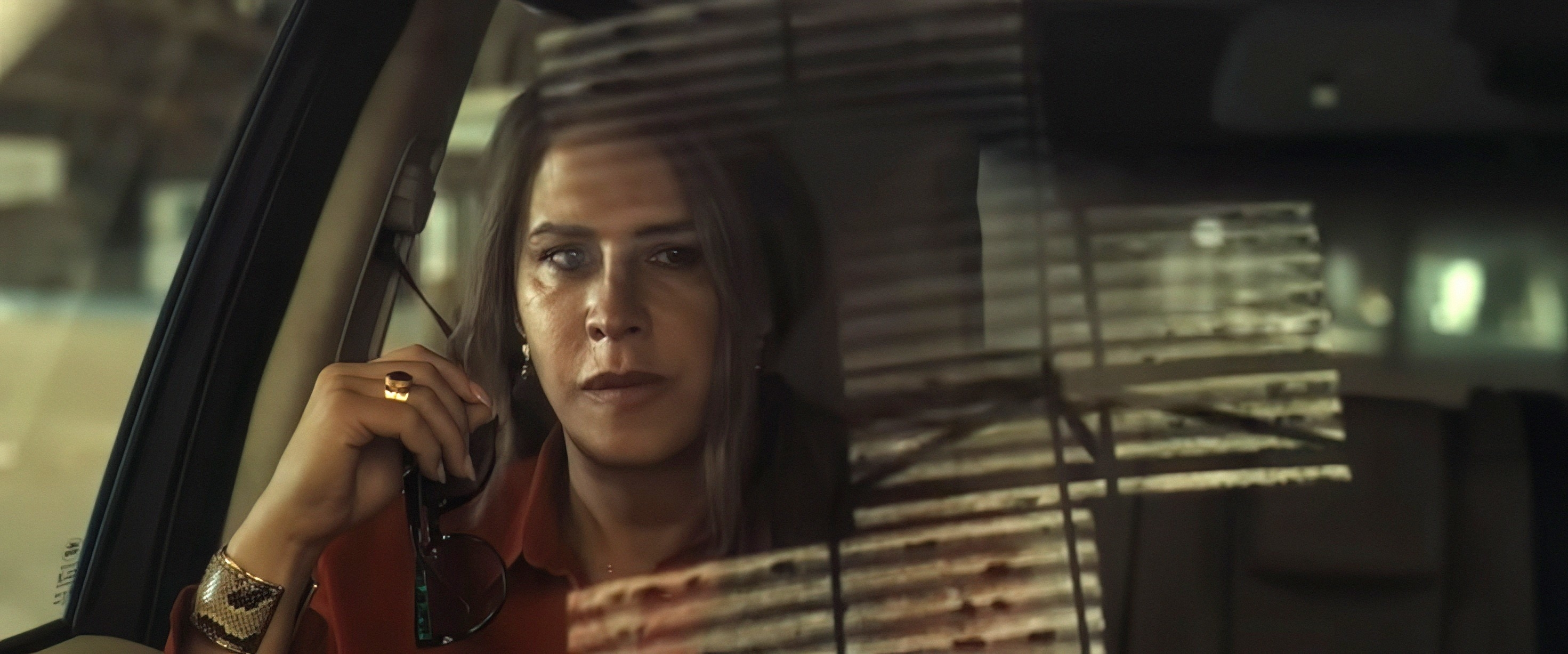 Person in a car looking out the window, holding glasses, with a serious expression