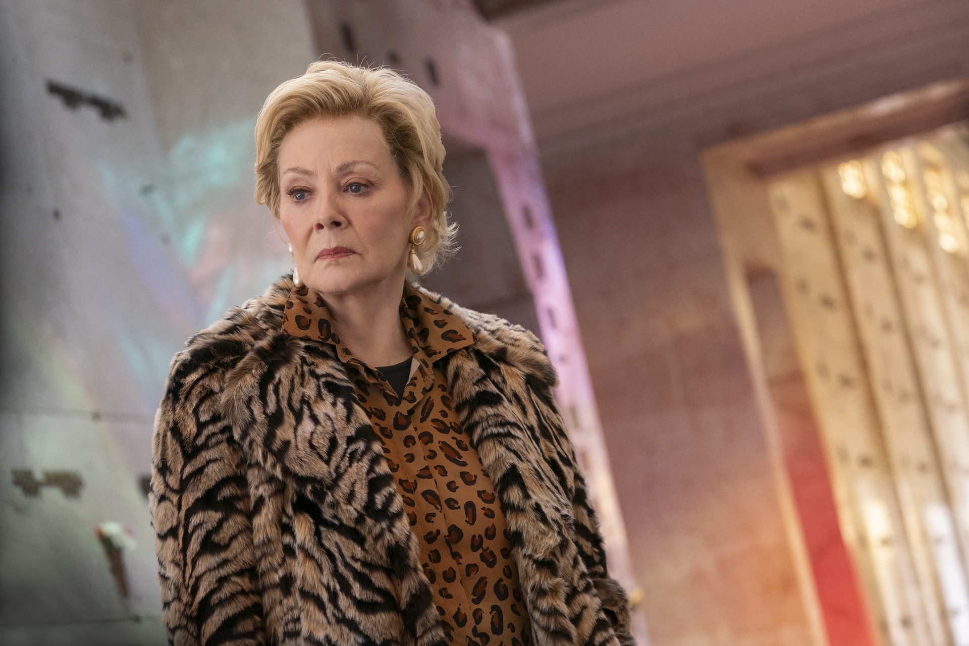 Person wearing a leopard print blouse and tiger stripe coat, standing indoors with a thoughtful expression