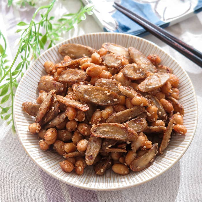 ごぼうと大豆の炒め物が盛り付けられた白い皿。背景には箸と植物の装飾が見える。