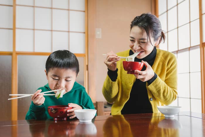 親子がテーブルで和食を楽しんでいる様子。笑顔で箸を使い、幸せな雰囲気。
